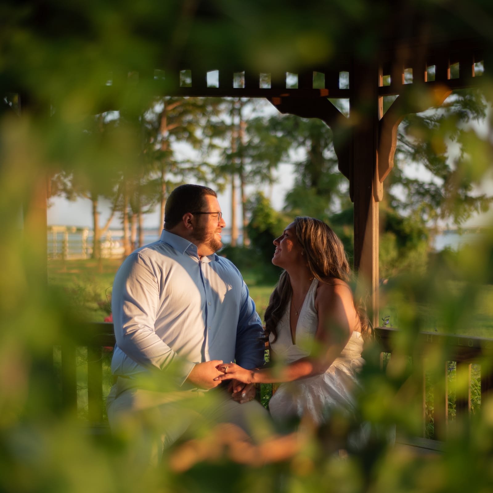 The couple seated in the gazebo, seen through a screen of leaves.